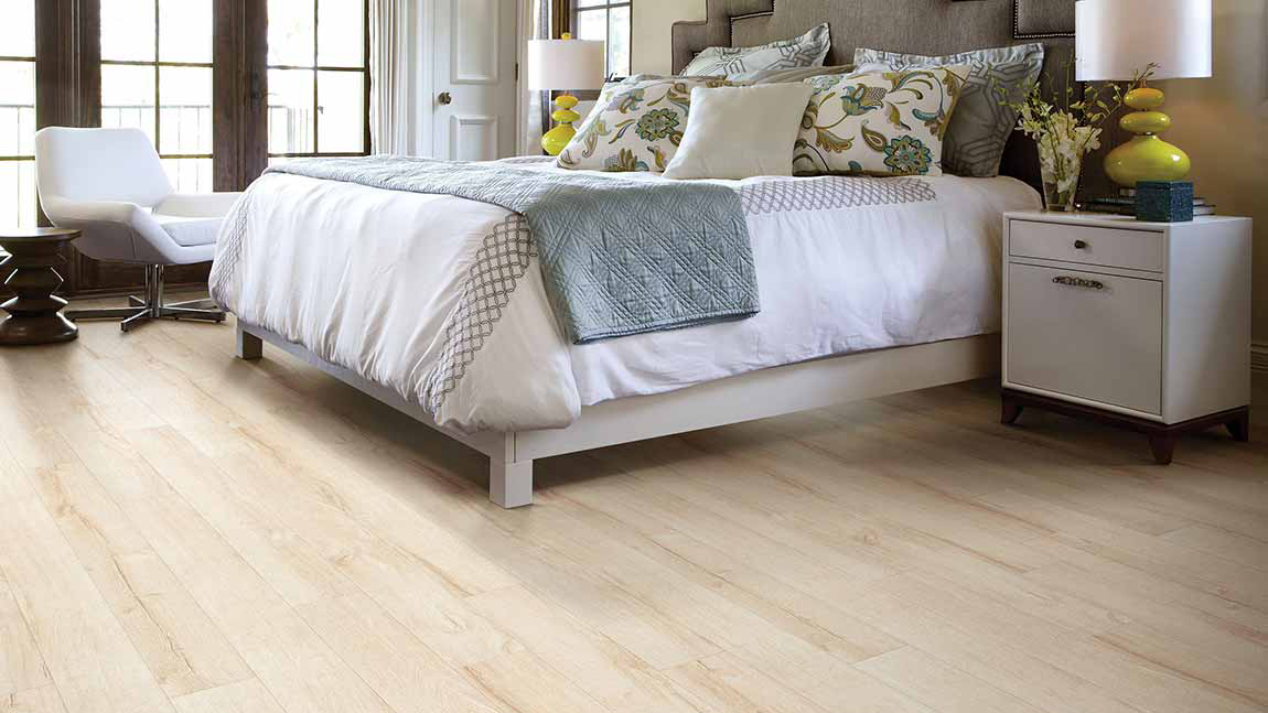 Wood-look laminate by Shaw Floors in bedroom scene with French doors, large bed and night stand